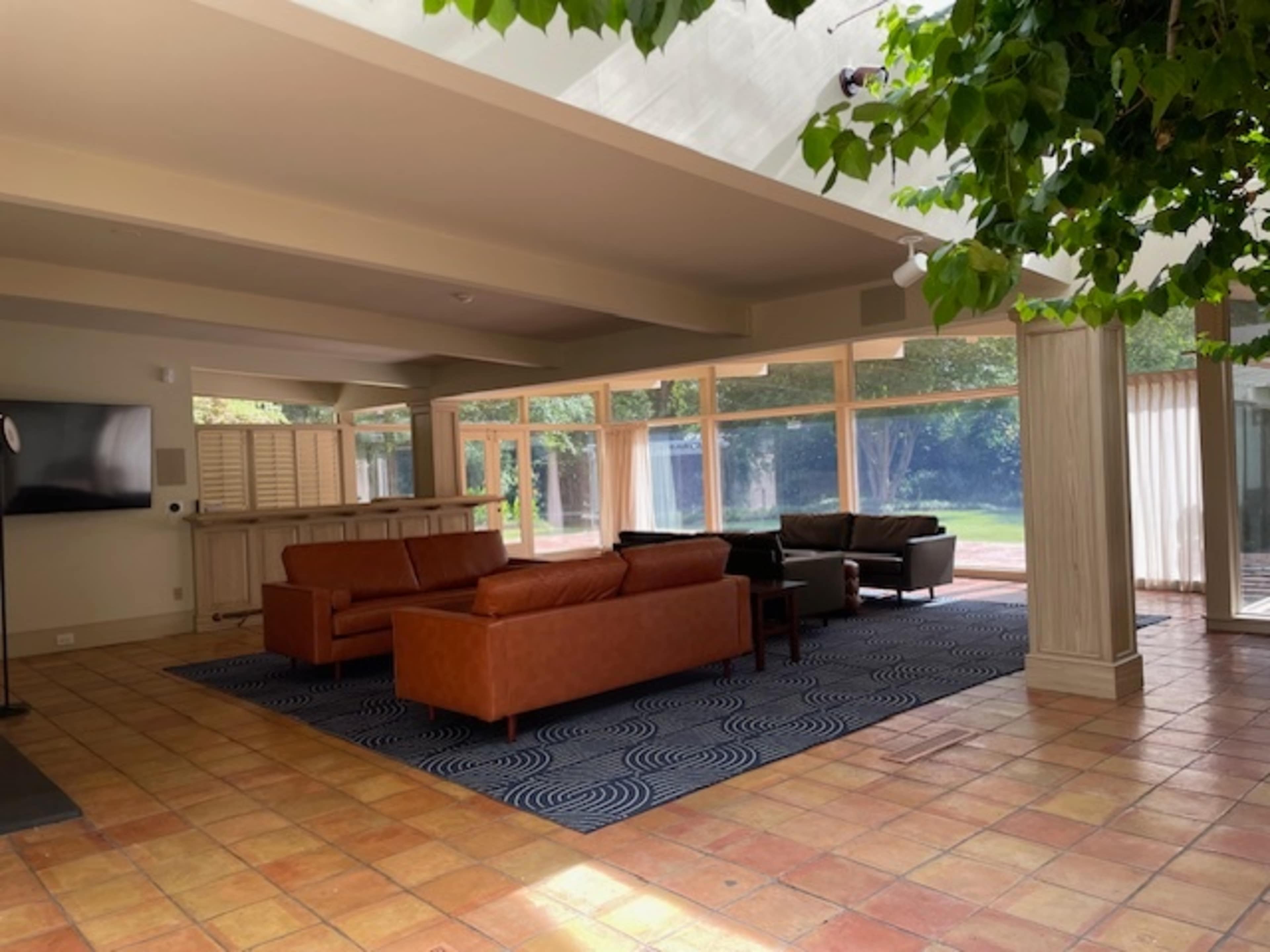 A spacious living area with two leather sofas, a rug, and large windows overlooking an outdoor space.