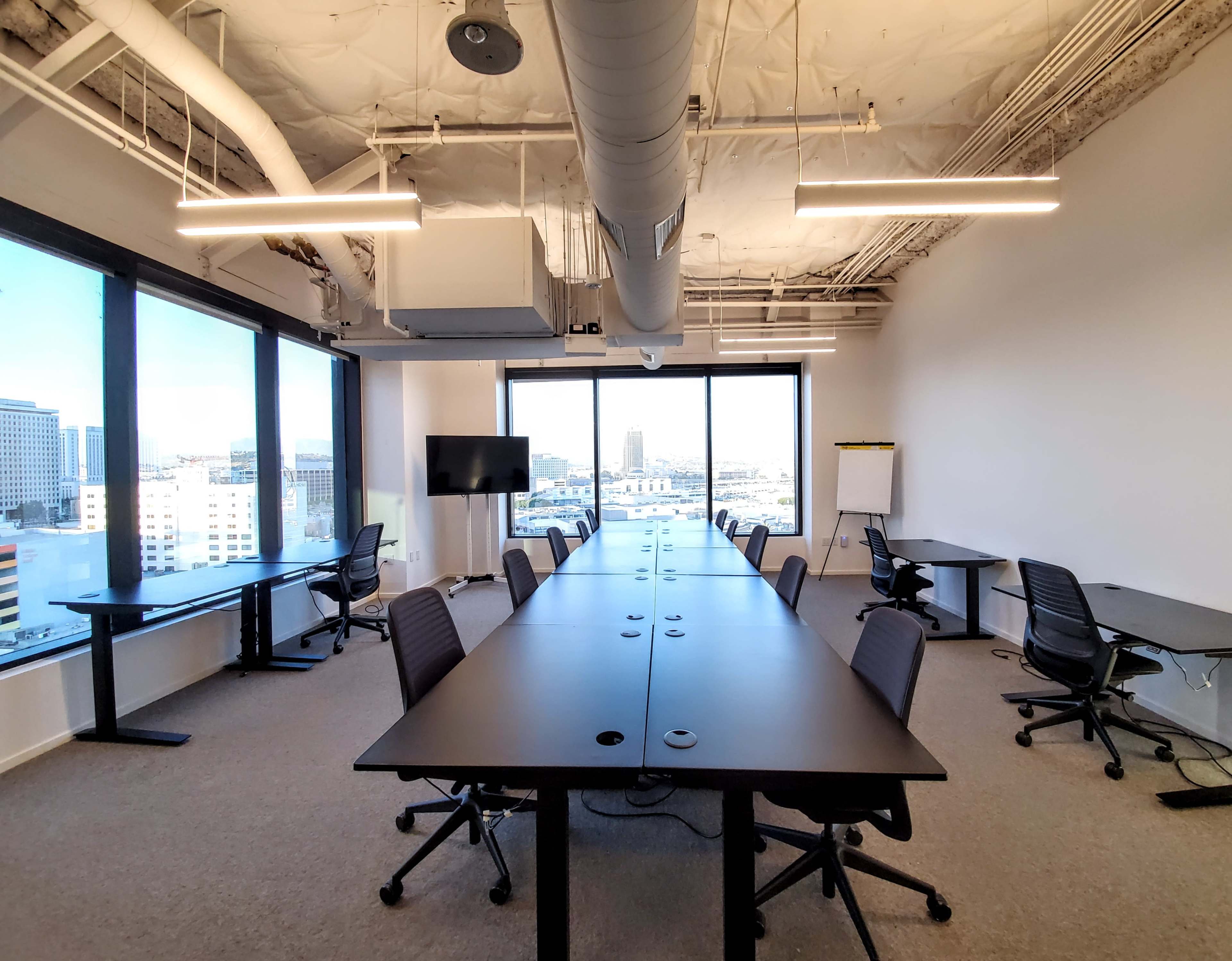 A modern conference room features multiple long tables with ergonomic chairs, large windows, and minimalistic decor.