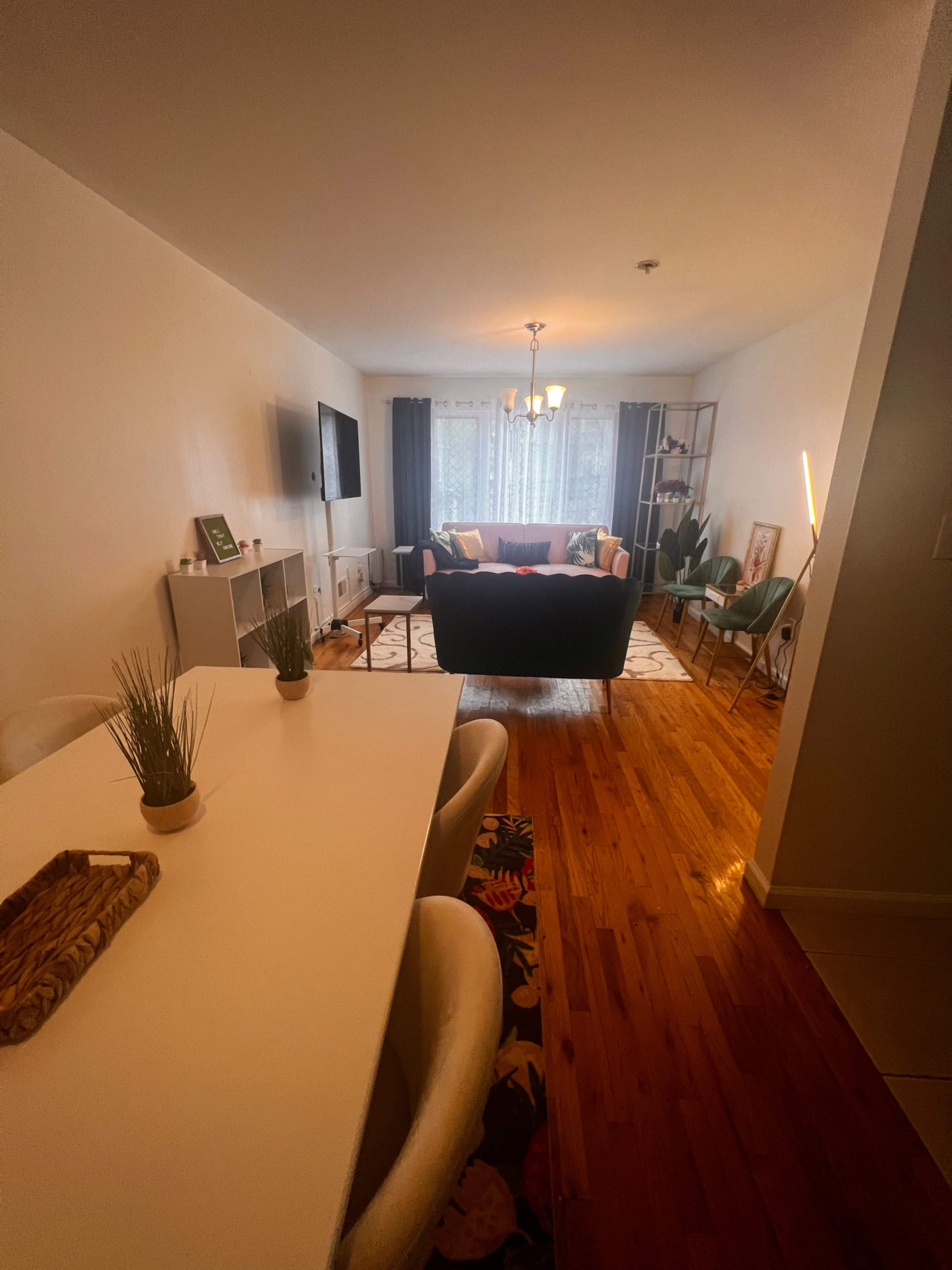 A modern living room is seen from an adjacent dining area, featuring a couch, a coffee table, and a television against one wall.