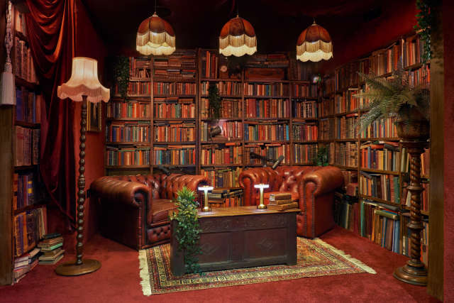 A cozy library podcast studio with leather couches, a wooden coffee table and walls lined with bookshelves at Fiction Studios Fitzrovia.
